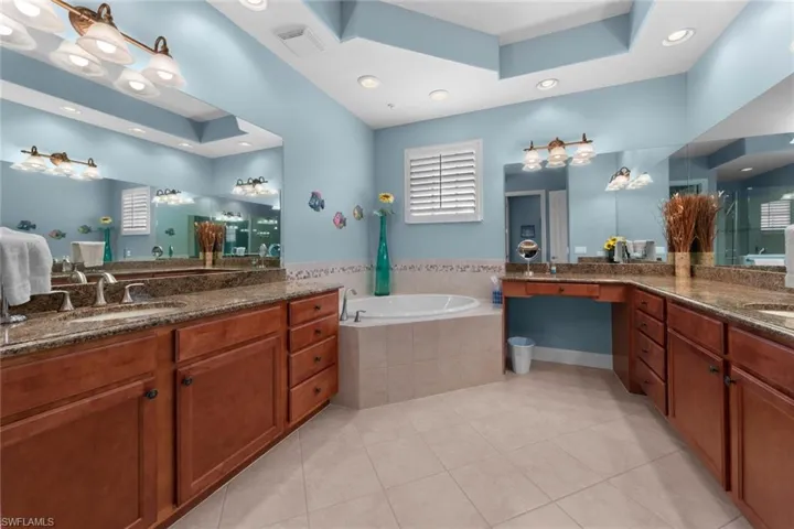 Bathroom featuring a relaxing tiled tub, vanity, tile patterned flooring, and a tray ceiling