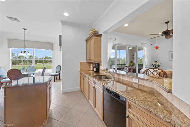 Kitchen featuring light tile patterned floors, ceiling fan with notable chandelier, light stone counters, black dishwasher, and sink