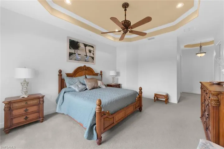 Bedroom featuring ceiling fan, light colored carpet, and a tray ceiling