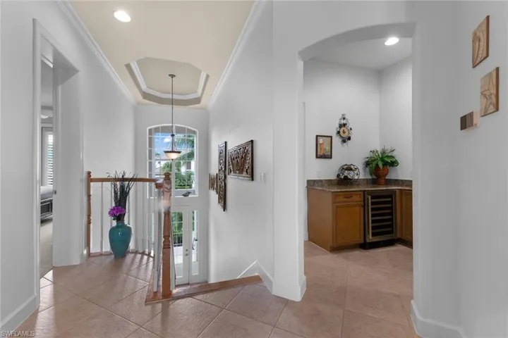 Hall featuring light tile patterned flooring, beverage cooler, a raised ceiling, and crown molding