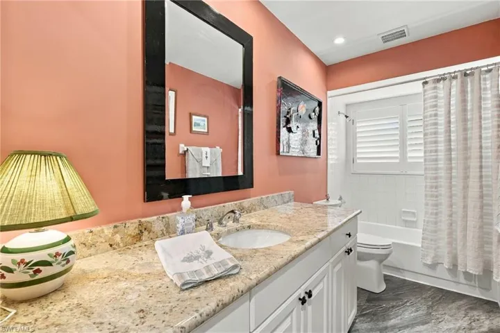 Granite-finish countertop with an undermount sink, white vanity cabinetry with dark hardware, and a framed mirror