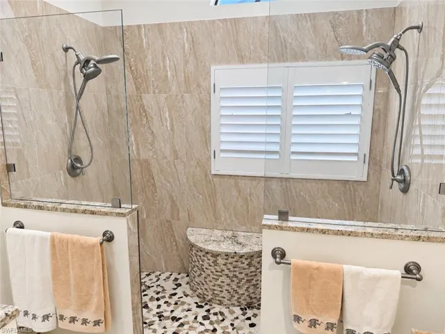 Dual shower system with handheld sprayers, natural stone tile surround, glass shower enclosure, mosaic tile shower floor, and plantation shutters