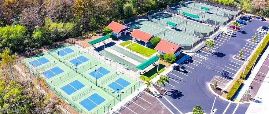 Multiple pickleball courts, several tennis courts, covered spectator areas, paved parking lot, and mature landscaping