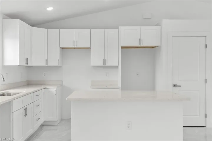 Kitchen with lofted ceiling, light marble finish floors, white cabinets, a kitchen island, and light stone counters