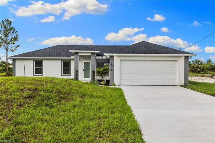 View of front facade featuring stucco siding, a garage, driveway, a front yard, and roof with shingles
