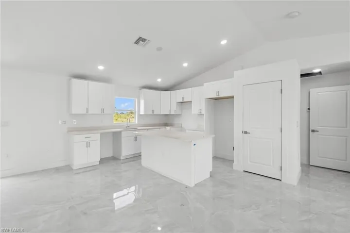 Kitchen featuring a kitchen island, vaulted ceiling, white cabinetry, light marble finish floors, and recessed lighting