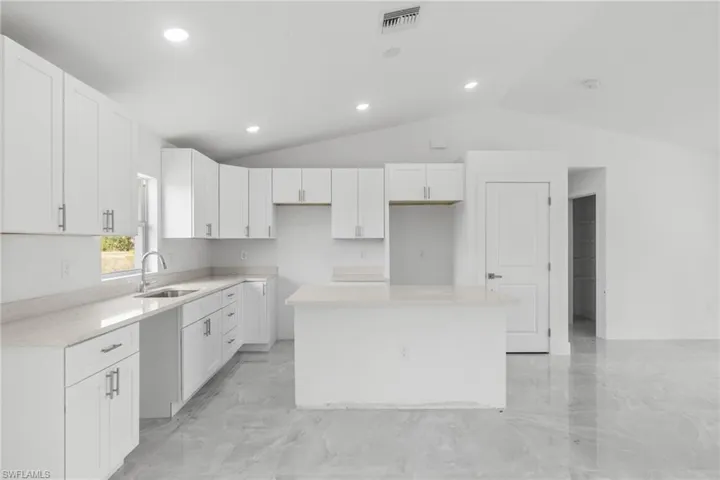 Kitchen with a center island, vaulted ceiling, white cabinetry, recessed lighting, and light marble finish flooring
