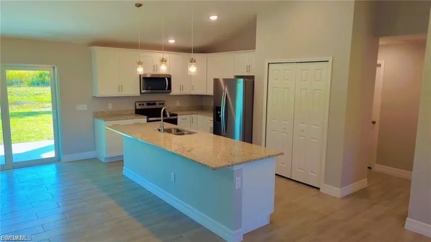 Kitchen featuring white cabinets, stainless steel appliances, light stone countertops, a center island with sink, and light wood-type flooring