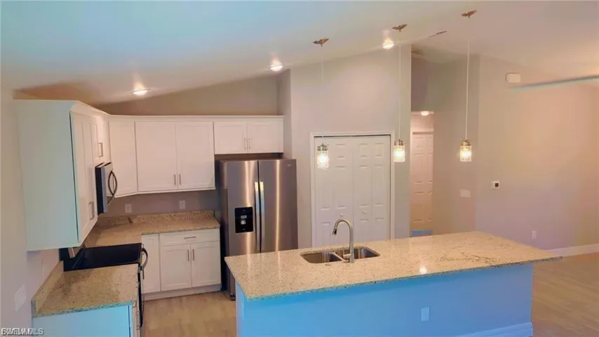 Kitchen with light stone countertops, lofted ceiling, light wood-style floors, stainless steel appliances, and white cabinetry