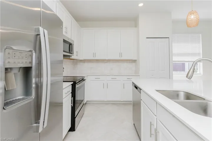 Stainless steel appliances, white cabinetry, integrated sink, and white countertops