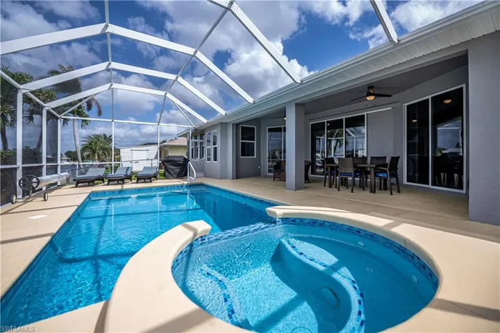 View of swimming pool featuring area for grilling, a patio, glass enclosure, ceiling fan, and a pool with connected hot tub