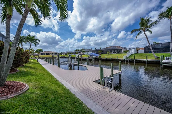 Newer composite wood dock area featuring a water view, boat lift, a residential view, and a lawn