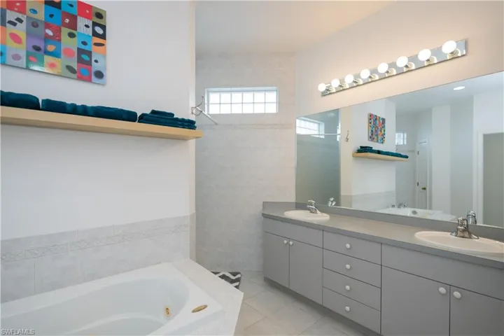 Full bathroom with tile patterned flooring, a sink, a tub with jets, and double vanity, walk through shower