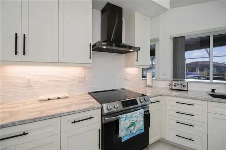 Kitchen featuring white cabinets, decorative backsplash, quartz counter tops, stainless steel range with electric cooktop, and wall chimney range hood