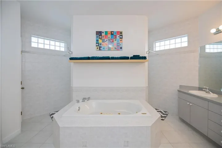 Full bath with a whirlpool tub, tile patterned flooring, double sink vanity, and tile walls, walk through shower, water closet