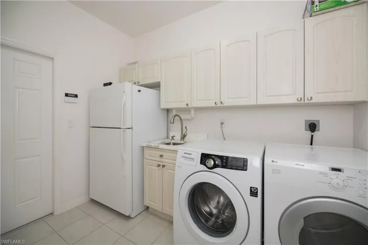 Clothes washing area with light tile patterned floors, a sink, and separate washer and dryer, extra storage