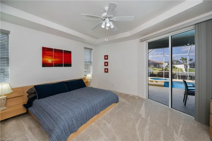 Bedroom featuring a ceiling fan, baseboards, access to exterior, a tray ceiling, and carpet