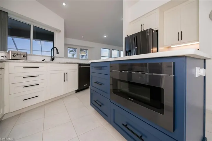 Kitchen featuring light tile patterned floors, recessed lighting, a sink, refrigerator with ice dispenser, and white cabinets with center island and built in drawer microwave
