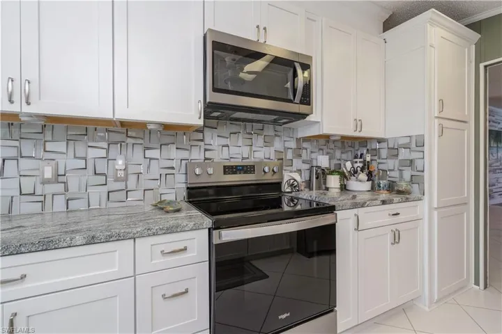 Kitchen featuring appliances with stainless steel finishes, light stone counters, white cabinets, light tile patterned floors, and a textured ceiling