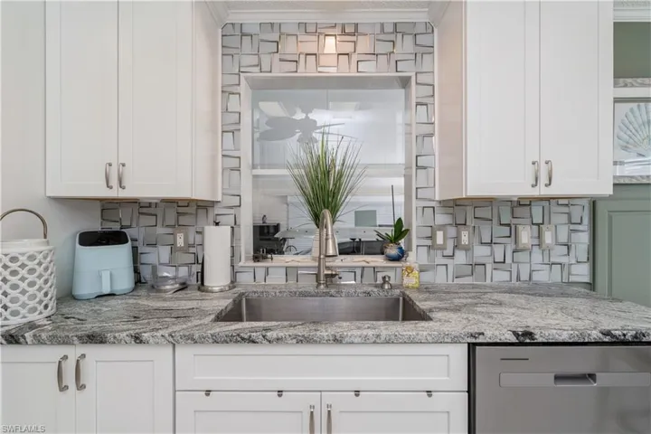 Kitchen featuring dishwasher, sink, decorative backsplash, and white cabinetry