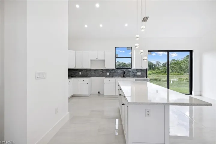 Kitchen featuring a center island, white cabinets, light stone counters, pendant lighting, and light tile floors