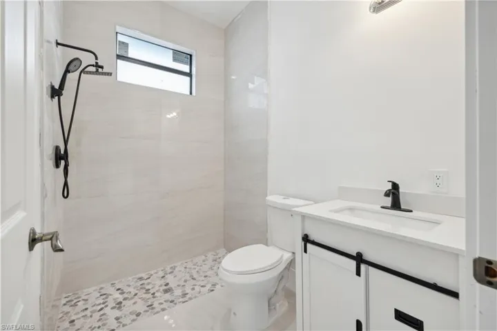 Bathroom featuring tiled shower, vanity, and toilet