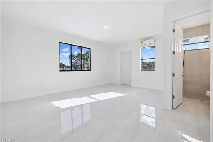 Unfurnished bedroom featuring multiple windows, ensuite bathroom, and light tile floors