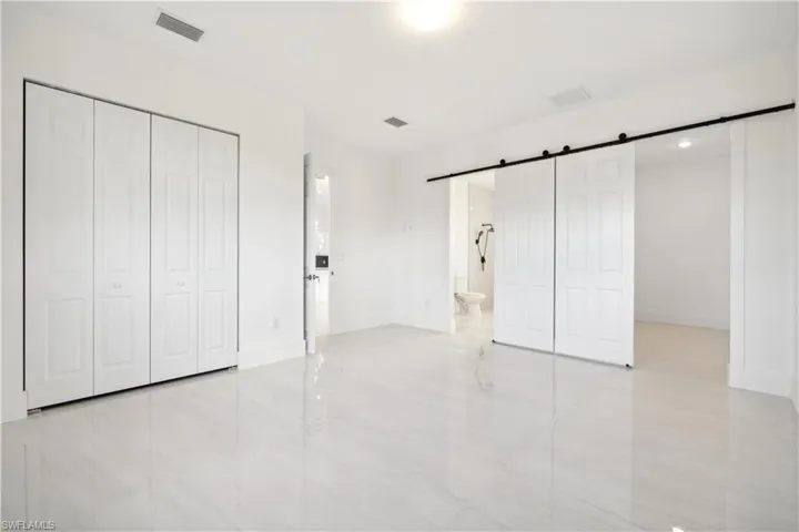 Unfurnished bedroom featuring a barn door, light tile floors, and ensuite bath