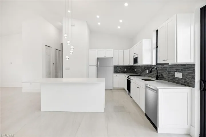 Kitchen with a kitchen island, stainless steel appliances, backsplash, hanging light fixtures, and sink