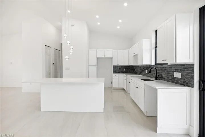 Kitchen with a center island, white cabinetry, hanging light fixtures, sink, and tasteful backsplash