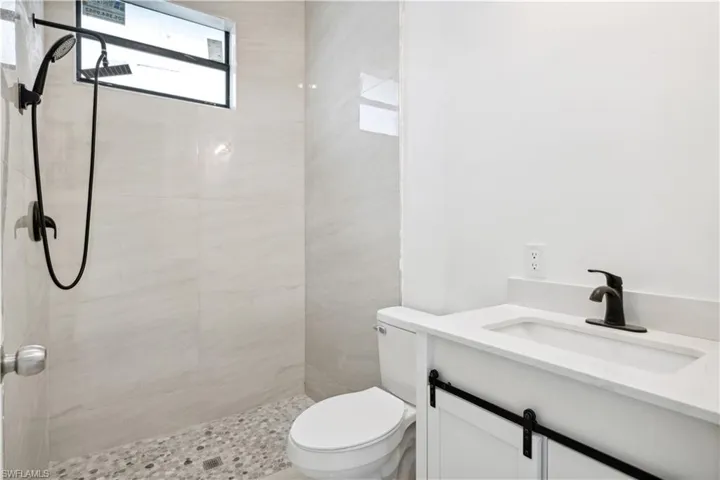 Bathroom with a tile shower, a wealth of natural light, toilet, and vanity