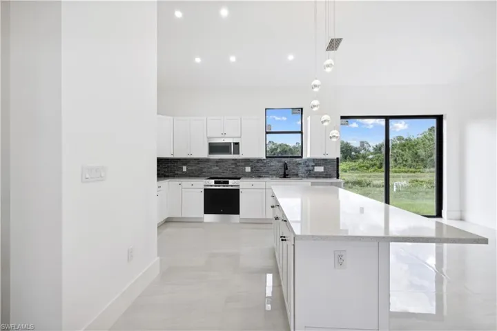 Kitchen featuring decorative light fixtures, light tile floors, a healthy amount of sunlight, white cabinets, and appliances with stainless steel finishes