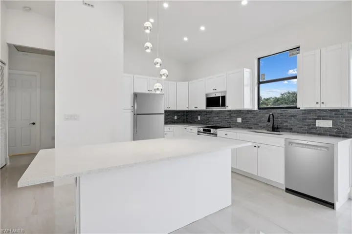 Kitchen featuring stainless steel appliances, a center island, tasteful backsplash, and decorative light fixtures