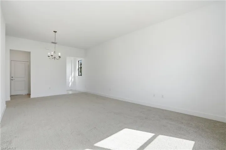 Unfurnished room featuring light colored carpet and a chandelier
