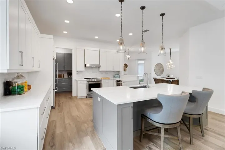 Kitchen with sink, decorative light fixtures, a large island with sink, stainless steel appliances, and white cabinets