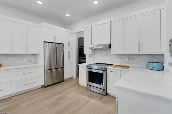 Kitchen featuring white cabinetry, tasteful backsplash, ventilation hood, appliances with stainless steel finishes, and light hardwood / wood-style floors