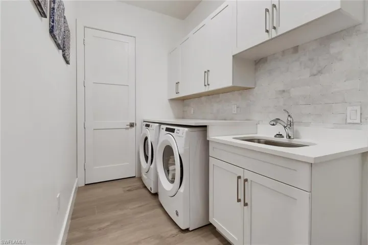 Laundry area with cabinets, washing machine and dryer, sink, and light wood-type flooring
