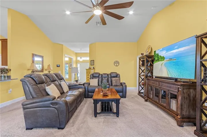 Living room featuring ceiling fan, light colored carpet, and lofted ceiling