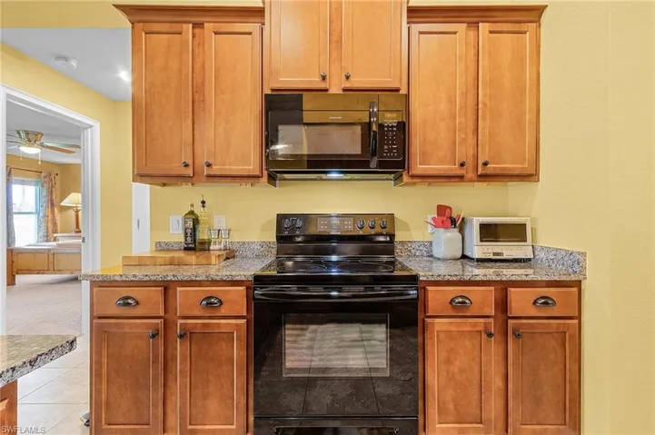 Kitchen with light stone counters, black appliances, ceiling fan, and light tile floors