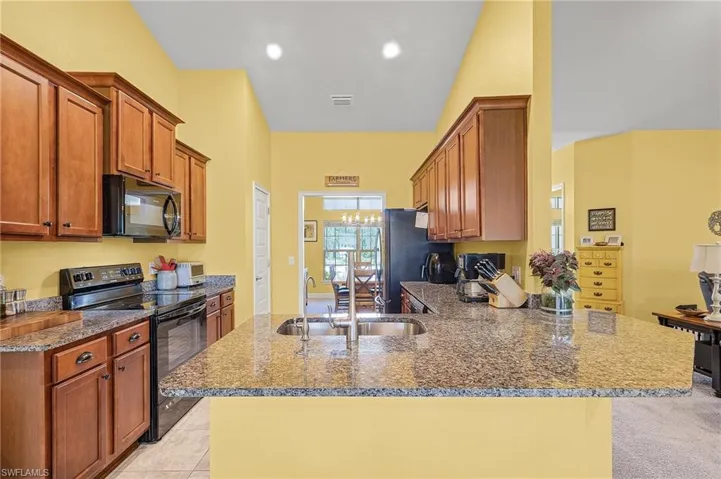 Kitchen featuring granite counters, soft close doors & pull-out racks, appliances, breakfast bar, all appliances, light colored tile floors, and sink with R.O.