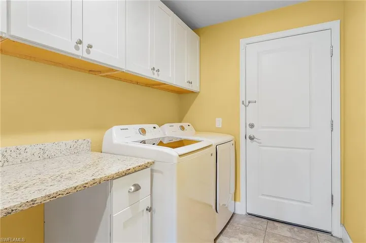 Clothes washing area with washer and dryer, cabinets, and light tile floors
