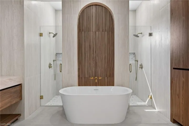 Full bath featuring a shower stall, vanity, a freestanding bath, and tile walls
