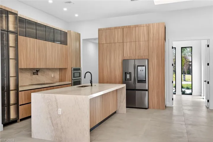 Kitchen featuring stainless steel appliances, an island with sink, light stone countertops, modern cabinets, and light wood finish cabinets