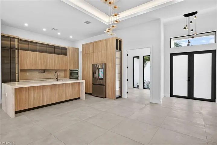 Kitchen featuring modern cabinets, light stone countertops, stainless steel fridge with ice dispenser, backsplash, and french doors