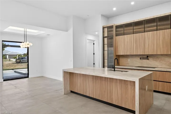Kitchen with light stone countertops, modern cabinets, backsplash, and hanging lights