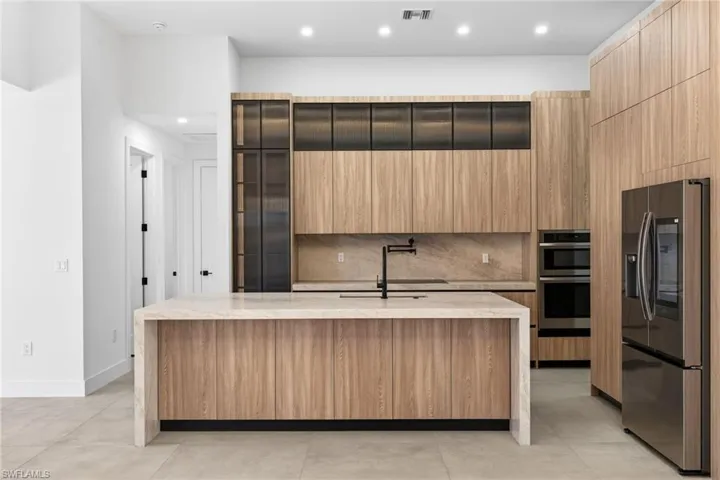 Kitchen featuring stainless steel appliances, light stone countertops, modern cabinets, a center island with sink, and recessed lighting