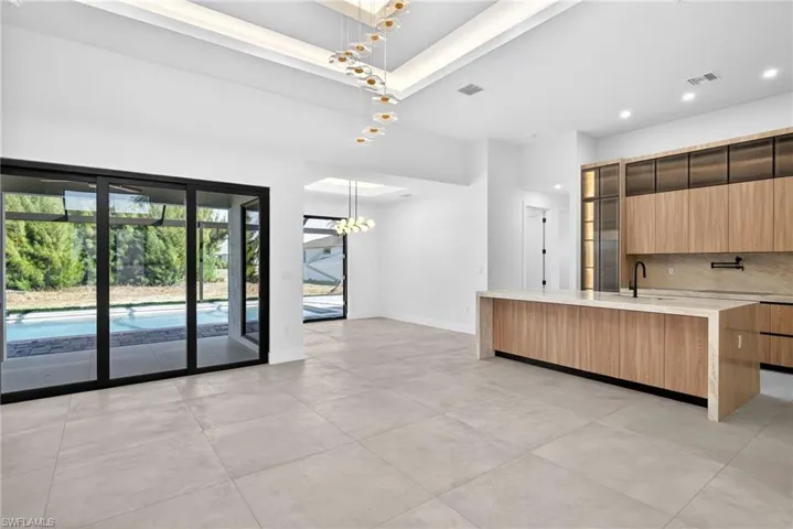 Kitchen featuring modern cabinets, light stone counters, hanging lights, a kitchen island with sink, and backsplash