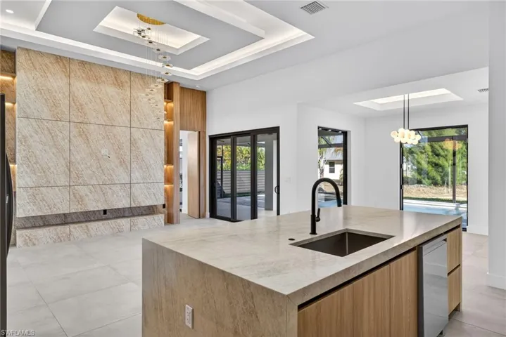 Kitchen with a raised ceiling, a skylight, hanging lights, light stone counters, and modern cabinets
