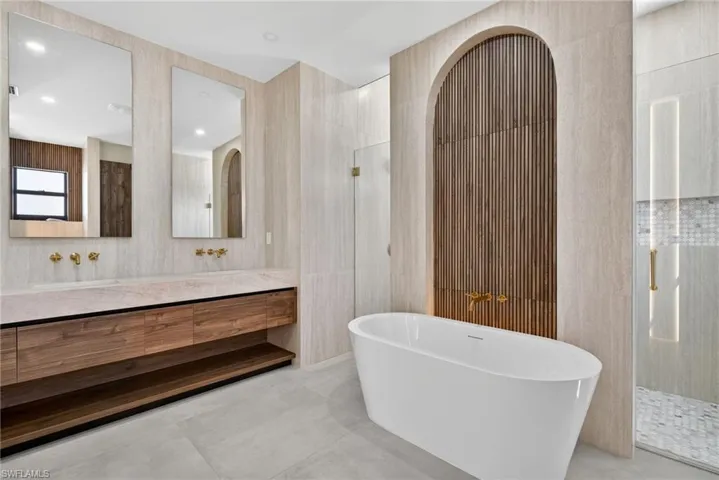 Full bath featuring a shower stall, tile walls, double vanity, and a freestanding tub