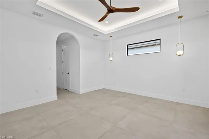 Unfurnished room with arched walkways, ceiling fan, and a tray ceiling